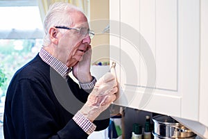Forgetful Senior Man With Dementia Looking In Cupboard At Home photo