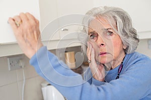 Forgetful Senior Woman With Dementia Looking In Cupboard photo