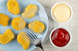 Fork on blue plate with chicken nuggets, bowls with ketchup and mayonnaise on wooden table. Top view