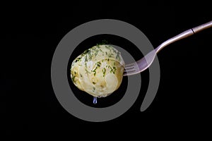 Fork with boiled young potato with dill and oil on a black background