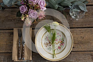 Fork and butter knife with plate and flower arranged on wooden table