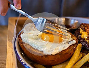 A fork cuts the egg yolk on a burger bun close-up