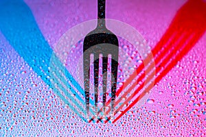 Fork with drops of water casting red blue shadows on white background. Fork tines close up. Silverware, stainless steel