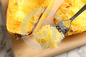 Fork with flesh of cooked spaghetti squash on blurred background