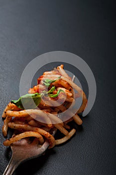 Fork full of twirled italian spaghetti with a bolognese meat sauce and basil.