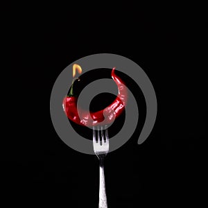 Fork impale to red hot chili on black photo