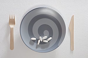 The Fork with knife and blank grey plate with pills on white background.