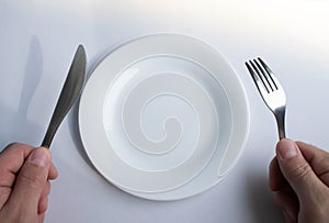 Fork and knife in hand against the background of an empty plate