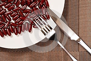Fork and knife with lots of capsules on dish concept of over-relying on medicine