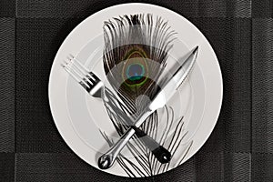 Fork & knife and a peacock feather on a dish concept of eating inhuman wildlife animal