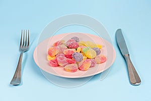 Fork, knife and pink plate with gummy candies isolated on blue