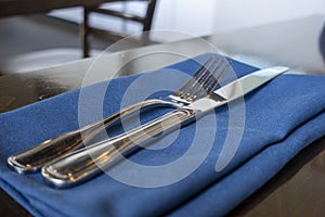 A fork and knife placed delicately on a royal blue cloth napkin on a wooden table inside a restaurant