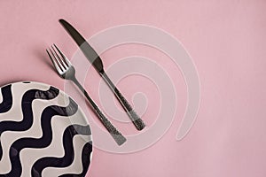 Fork and knife on a striped plate on a pink background, table setting