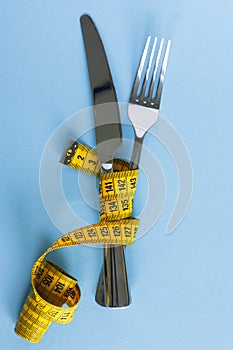 Fork and knife wrapped in tape-line on blue background. Diet concept.