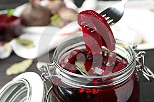 Fork with pickled beets over glass jar on table, closeup