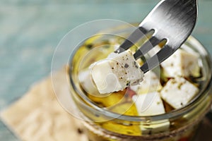Fork with pickled feta cheese over jar on blue table