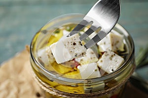 Fork with pickled feta cheese over jar on blue table