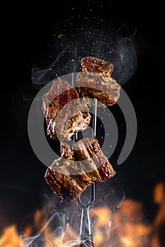 Fork with pieces of delicious barbecued meat on black background