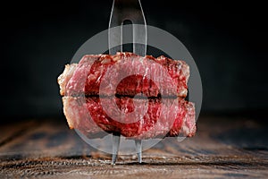 Fork with pieces of grilled striploin beef steak stuck in a wooden table