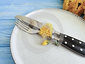 Fork, plate, knife design yellow chrysanthemums on a blue wooden background