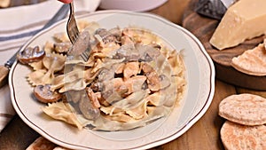 A fork in a plate with pasta. Butterfly pasta with mushrooms and parmesan cheese sauce. Typical italian cuisine from the