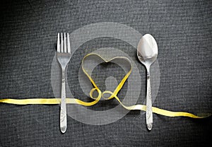 Fork and spoon with heart shape made from yellow ribbon on black