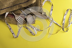 Fork, spoon,knife and measurement tape with yellow background, diet or healthy eating concept. Soft focus at the middle