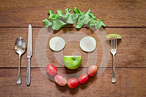 Fork,spoon,knife and smiling shaped salad vegetables on grunge wooden background