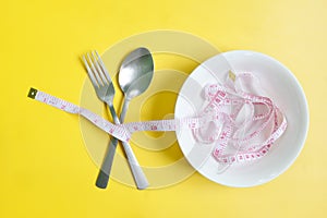 Fork and spoon wrapped with measuring tape flat lay in yellow background. Anorexia, Diet and nutrition to lose weight concept.