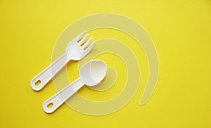 Fork and spoon on a yellow background. Plastic utensils. Tableware for games. Meals, lunch. Children is set of dishes