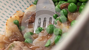 A fork stuck in a bowl full of cottage pie and peas