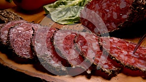 Fork takes a piece of uncooked jerked sausages from a wooden board