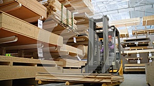 Forklift driver in protective vest driving forklift at lumber warehouse