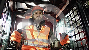 Forklift driver in protective vest driving forklift at warehouse of freight forwarding company. Man on the forklift