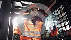 Forklift driver in protective vest driving forklift at warehouse of freight forwarding company. Man on the forklift