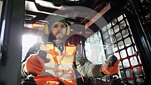 Forklift driver in protective vest driving forklift at warehouse of freight forwarding company. Man on the forklift