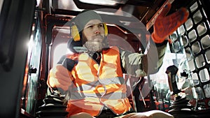 Forklift driver in protective vest driving forklift at warehouse of freight forwarding company. Man on the forklift