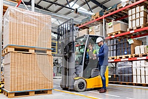 Forklift driver talking with manager in modern industrial factory. Woman warehouse worker discussing order, order