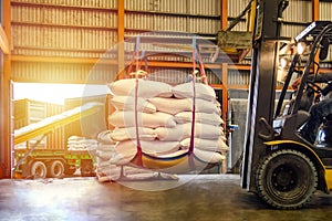 Forklift handling white sugar bags for stuffing into containers outside a warehouse.