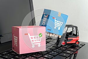 Forklift lift parcel carton box with shopping trolley cart logo on laptop computer with white wall background. E-commerce