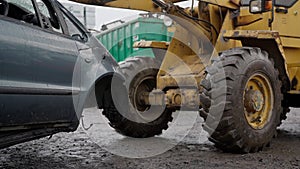 Forklift stacks cars into pile in junk yard tidying up vehicles in rainy weather