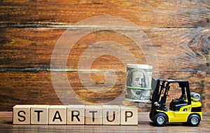 Forklift truck carries a bundle of dollars to inscription Startup. The concept of raising funds for a startup. Crowdfunding