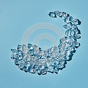 Transparent ice cubes in the shape of a dolphin on a blue background. Top view