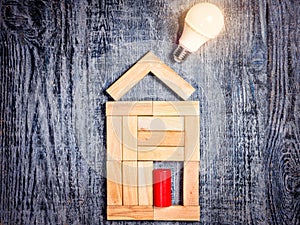 Form of house above tree on dark wooden background and LED bulb. Imitation of heating copper or boiler and air conditioner