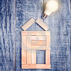 Form of house above tree on dark wooden background and LED bulb. Imitation of heating copper or boiler and air conditioner