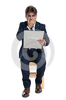 Formal businessman sitting and reading the newspaper terrified