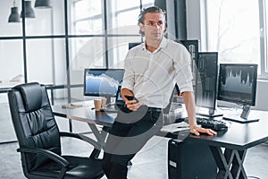 In formal clothes. Young male stock brocker works indoors in the office. Many of displays photo