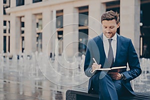 Formally dressed office worker organising his day in note book while working outdoors