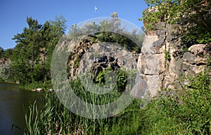 Former stone quarry. Summer landscape with a river, rocks, green grass, trees, and blue sky.