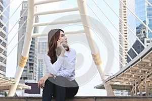 Fornt view of beautiful young Asian woman sitting and talking on phone at urban city background.